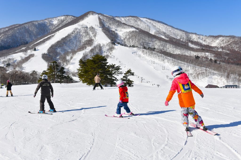 Ski instructor teaching children on the slopes of an Iiyama ski resort with snowy mountains