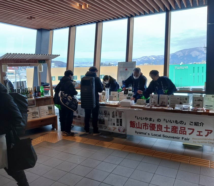 Visitors browsing a local souvenir fair inside a modern building with large windows overlooking snowy mountains.