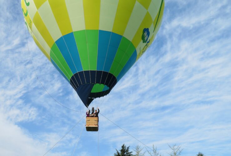 A colorful hot air balloon against a blue sky with passengers waving from the basket