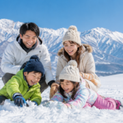 雪山を背景に親子4人が雪遊びを楽しむ冬の家族旅行風景