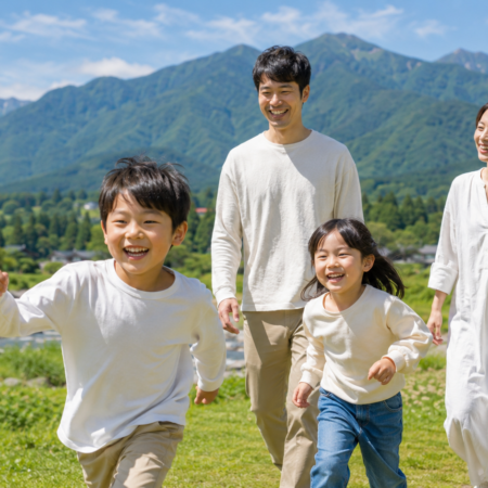 長野県飯山市の緑豊かな山々と川沿いを笑顔で歩く家族4人