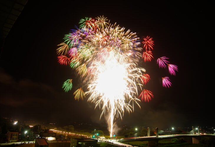 千曲川河畔で打ち上げられる色とりどりの花火、橋と夜景を背景に